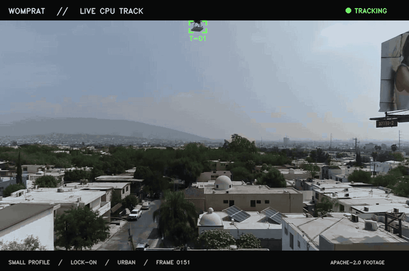 Womprat keeping a green tracking box on a drone crossing an urban rooftop and city skyline.