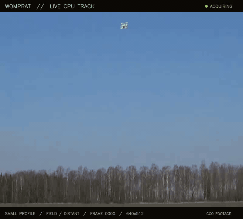 Womprat holding a green tracking box on a small white drone flying over a distant tree line.